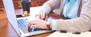 Photo of a person typing on a computer, image is cropped so we only see hands on the keyboard.